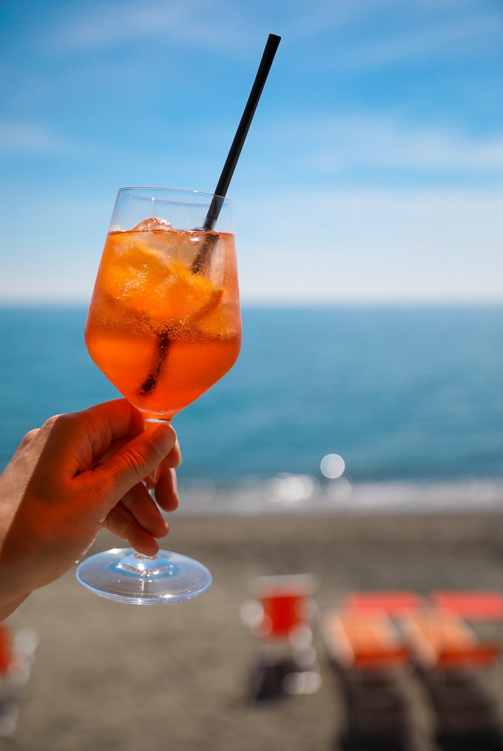 Holding up a cold glass of Aperol Spritz while relaxing on a beach in Ischia. Find the best restaurants and bars in this guide to Ischia, Italy.