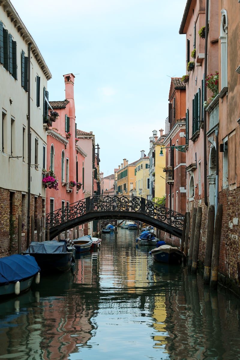 A colorful, peaceful canal in Venice with boats docked along the side