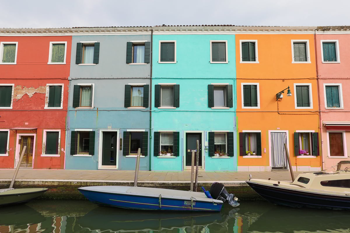 Boats in front of pastel-colored houses by a canal in Burano, Venice