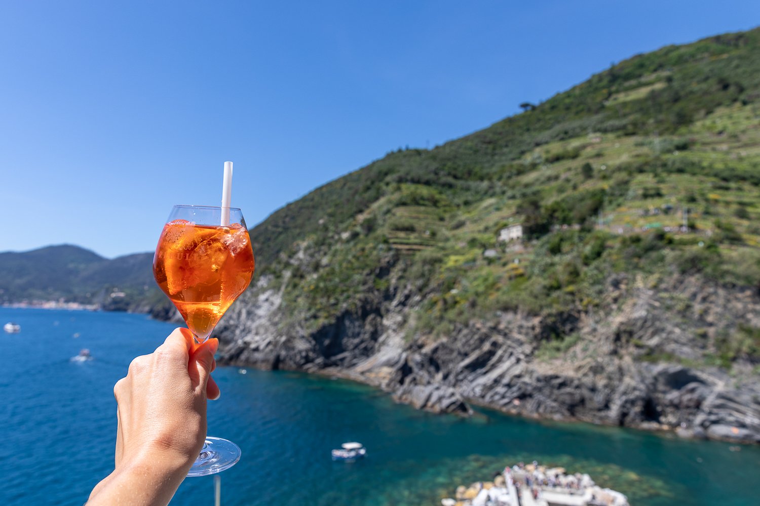 Holding up an Aperol spritz with sea and rocky coastline in the background