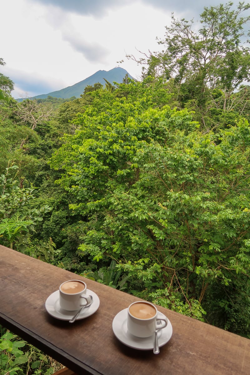 Two cups of coffee on a wooden deck overlooking the lush jungle trees in La Fortuna