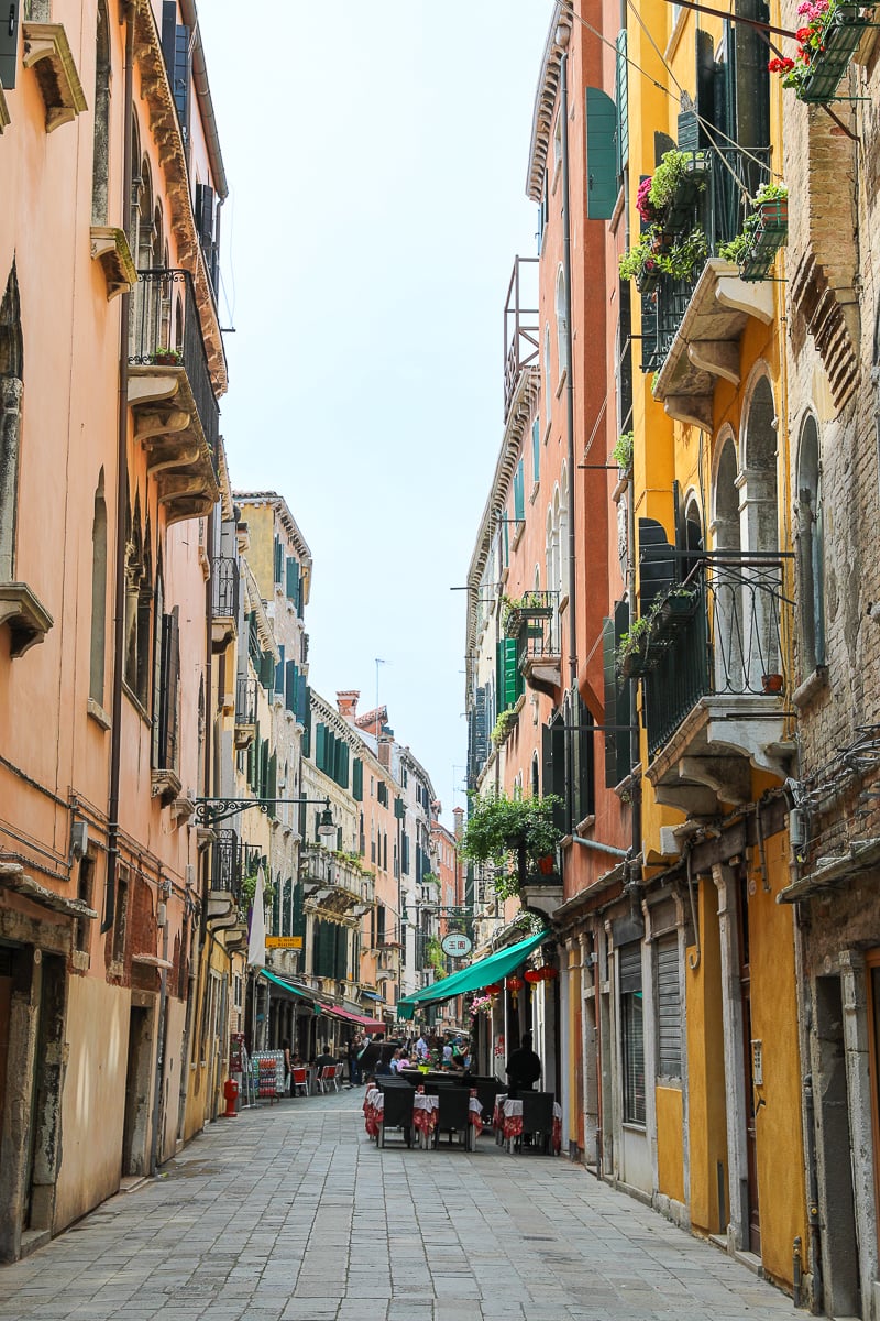 A street in Venice lined on both sides with old and colorful homes, shops, and restaurants