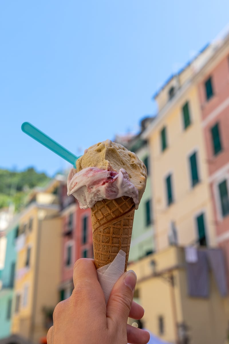 Maddy holding up an ice cream cone with the colorful houses of Cinque Terre in the backdrop