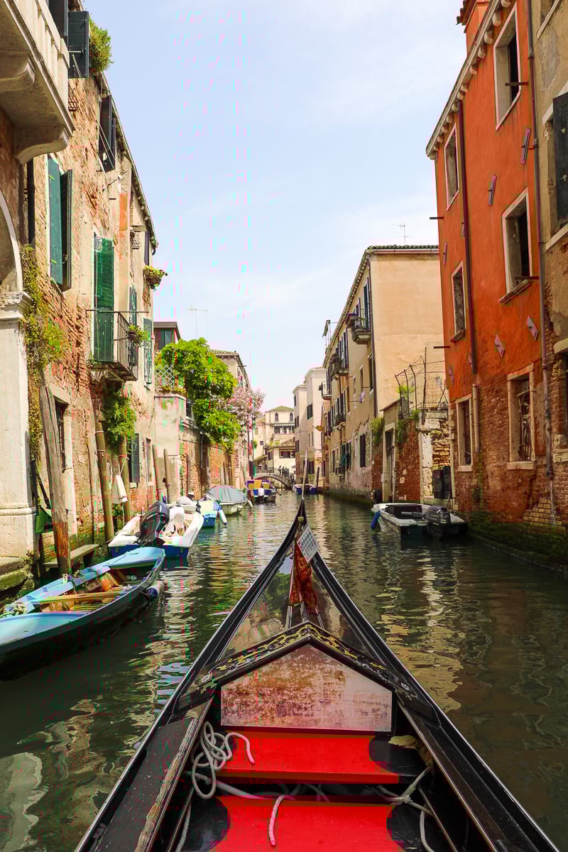 The front of a gondola boat cruising along a colorful canal in Venice