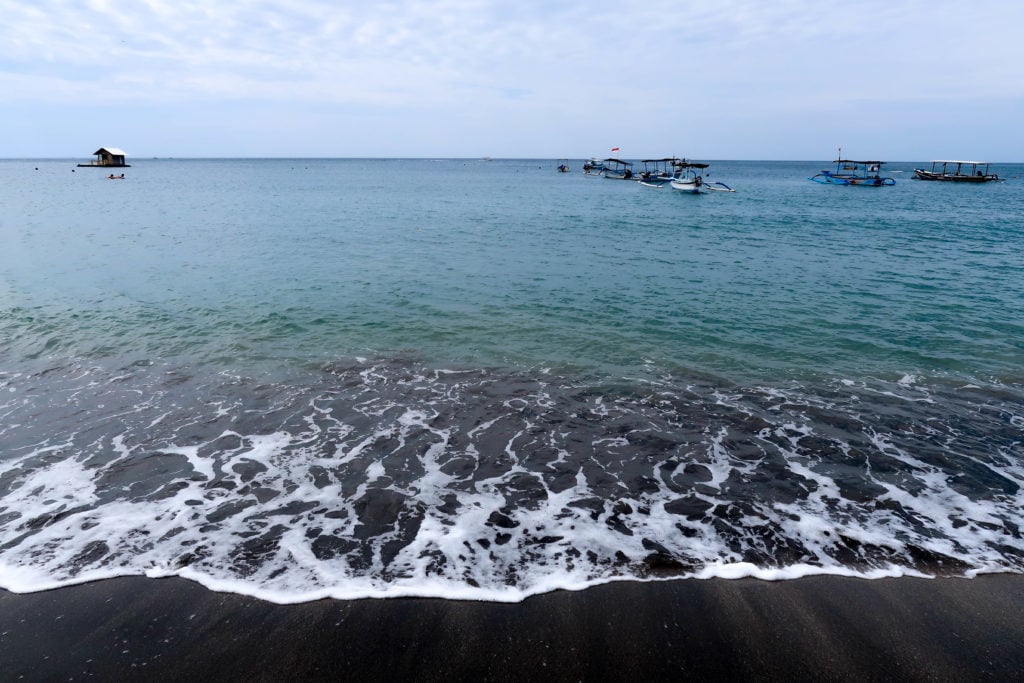 Black sand beach with boats floating on the water in Pemuteran