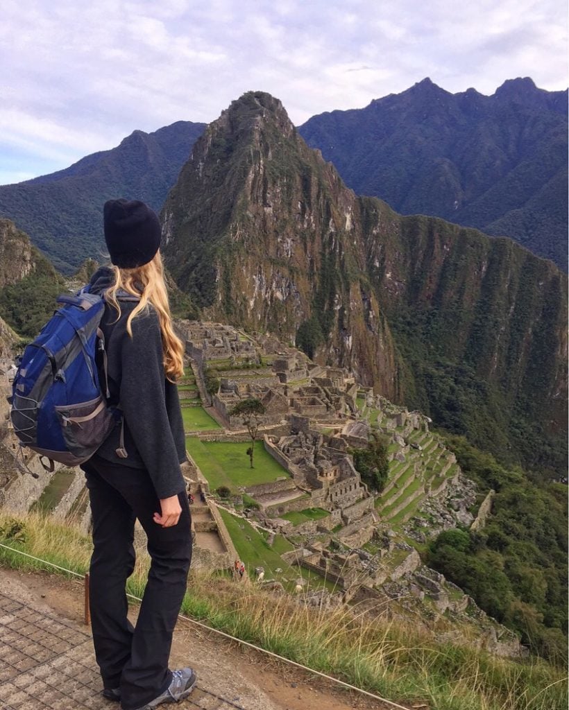 Maddy standing on Inca Trail while staring at the historical Machu Picchu heritage site. In this guide, you'll find a well-curated Machu Picchu packing list.