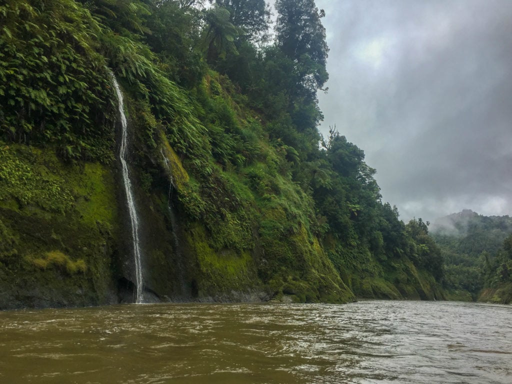 Waterfall rushing down the lush cliff side to the river on a cloudy day