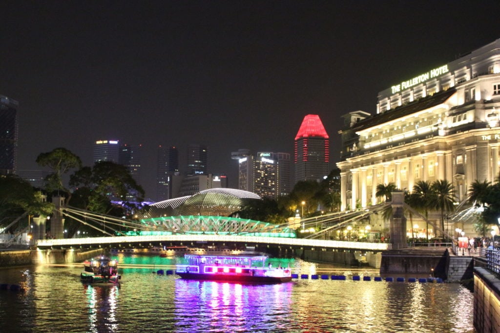 Colorful, lit boats on a lake under a bridge. This guide to a 24-hour layover in Singapore covers what you need to know before you go.