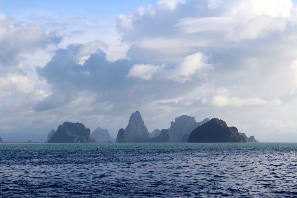 Silhouettes of islands and rock formations under cloudy skies. In this guide to Phuket, you'll learn about the best places to visit in Phuket, Thailand.