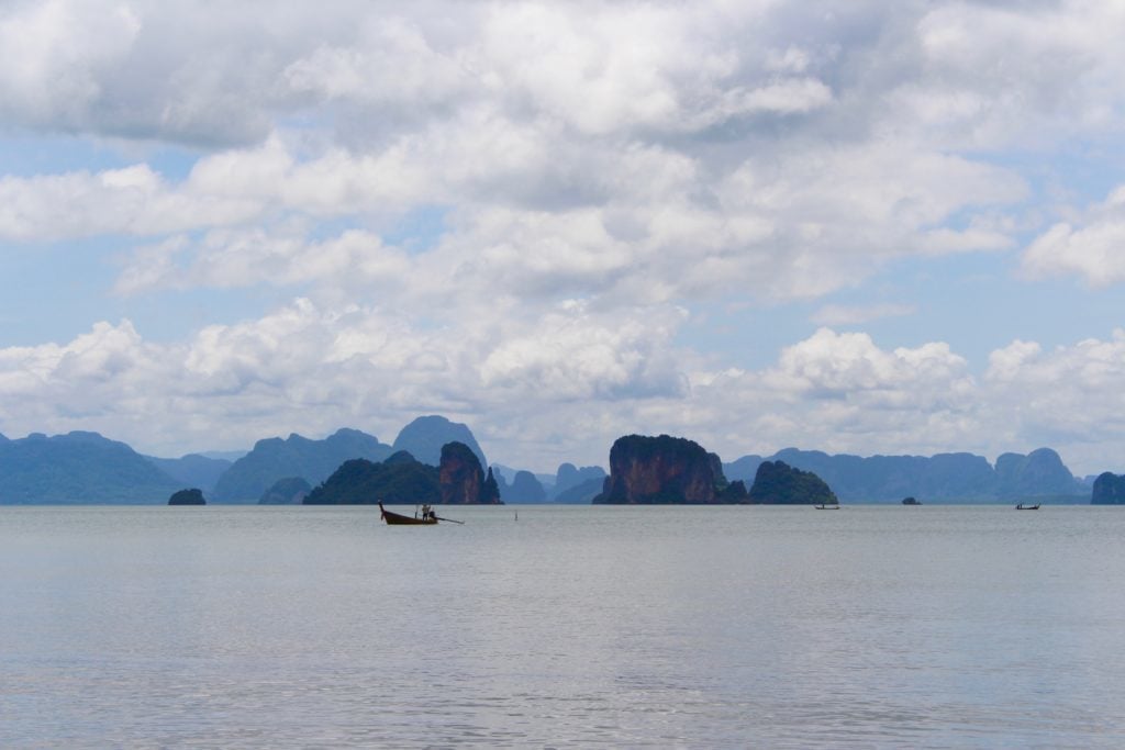 Small boat in the middle of the sea surrounded by beautiful rock formations on a cloudy day