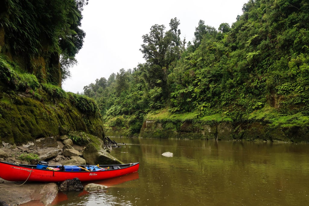 Red canoe docked on the nearby rocky ground by the river. In this ultimate guide to the Whanganui River Journey, we'll share our experience of this epic three-day adventure.