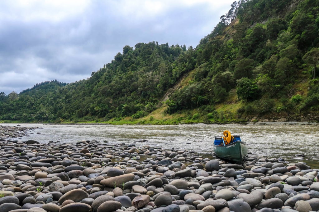 Green canoe docked on a riverbank filled with stones