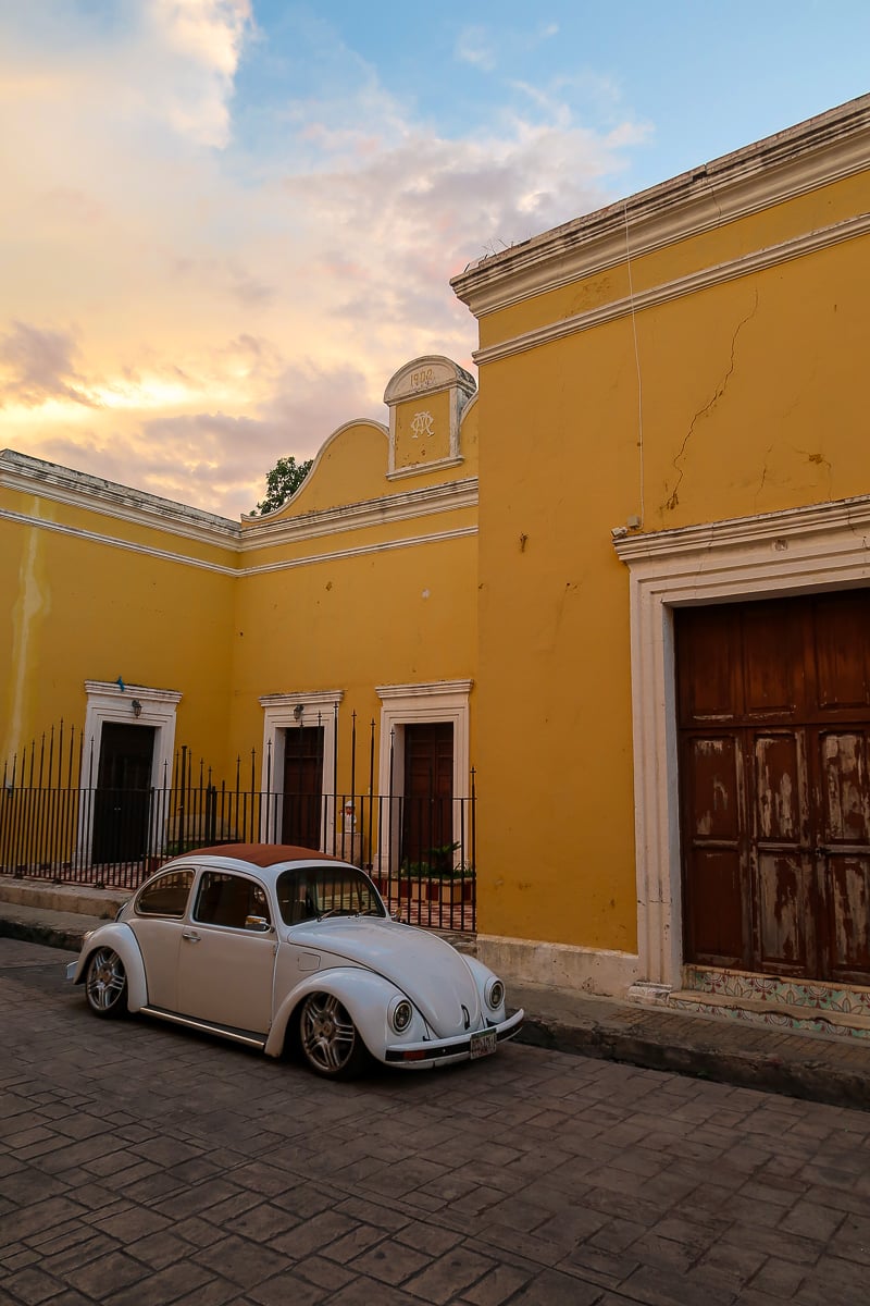 White car parked by a yellow building in Izamal. Find the best things to do in Izamal in this guide.