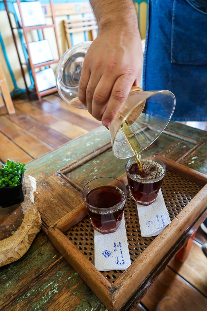 Freshly-brewed dark coffee being poured in two short glasses on a wooden tray at Cafe Jesus Martin
