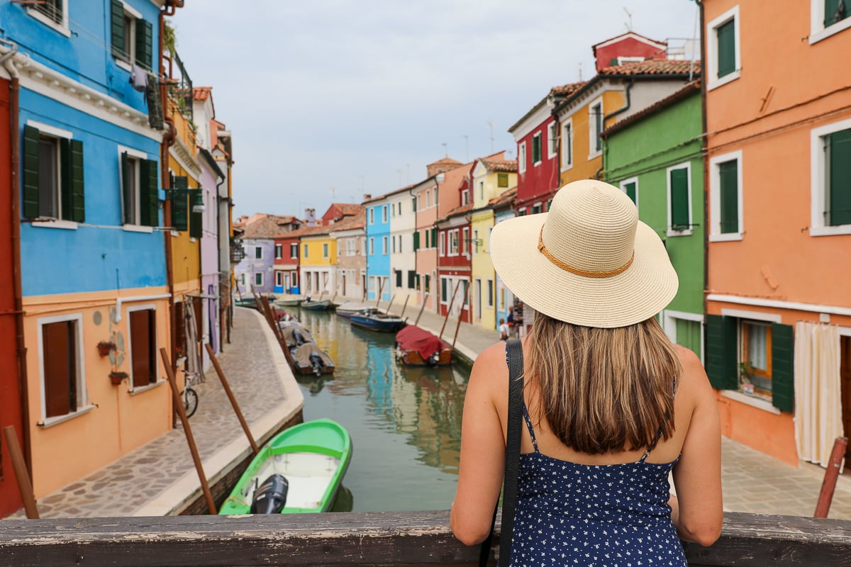 Maddy standing on a bridge overlooking a colorful street in Burano, Venice, Italy. Visiting Burano is one of the best things to do during 2 days in Venice!