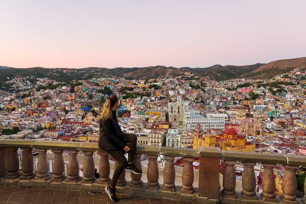 Maddy in Guanajuato, with the panoramic view of colorful buildings of Guanajuato and hills on the background