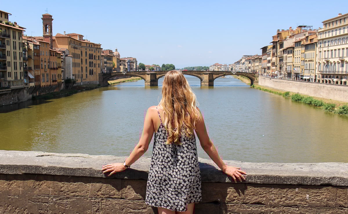 Maddy, blogger, on a bridge in Florence while admiring the views of medieval buildings lining the river