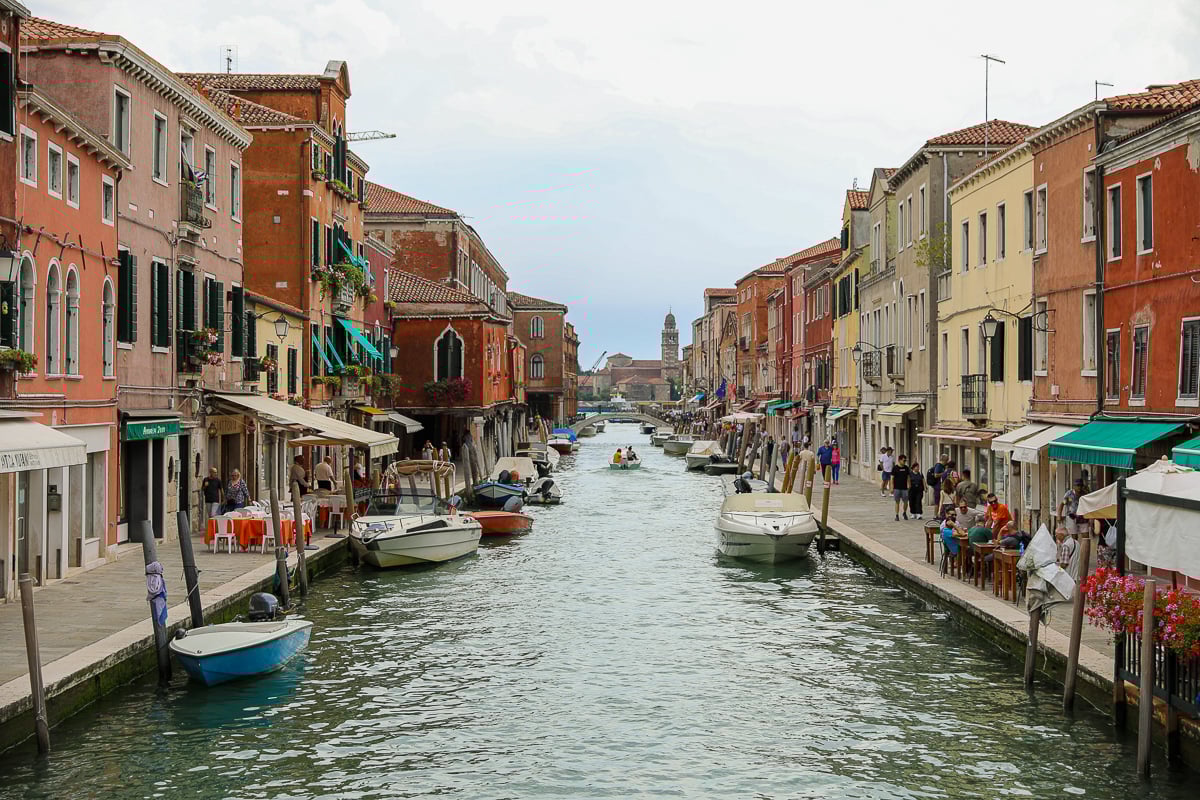 Quaint buildings and stores by a canal in Murano. If you're visiting Murano and Burano in one day, this ultimate guide tells you everything you need to know.
