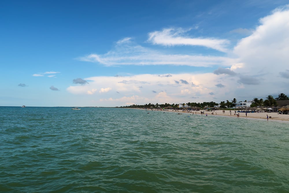 Emerald waters, white-sand beach, and partly cloudy blue skies in Sisal. One of the best things to do in Sisal is go on adventure tours to witness the town's beautiful sights.