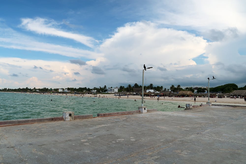 Emerald waters and white-sand beach near a pier. Seeing the historic sites is one of the best things to do in Sisal, Yucatan.