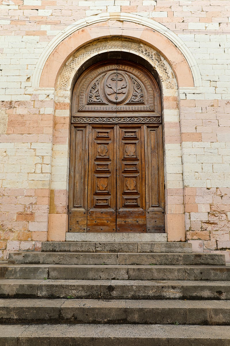 Stone stairway leading up to a wooden arched door in Spello, Italy