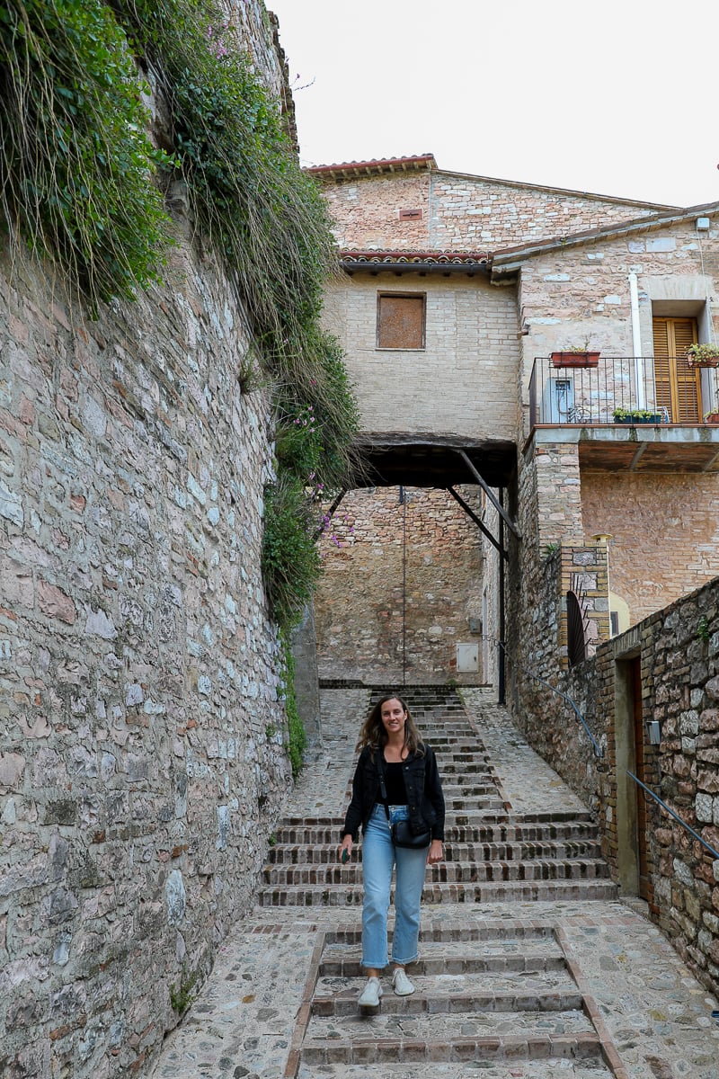 Maddy strolling along the streets of Spello with old stone walls and stairways