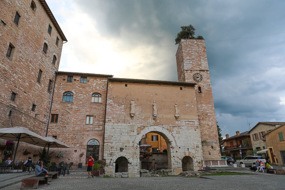 Main piazza of Spello, with a clock tower with trees and bells on the roof