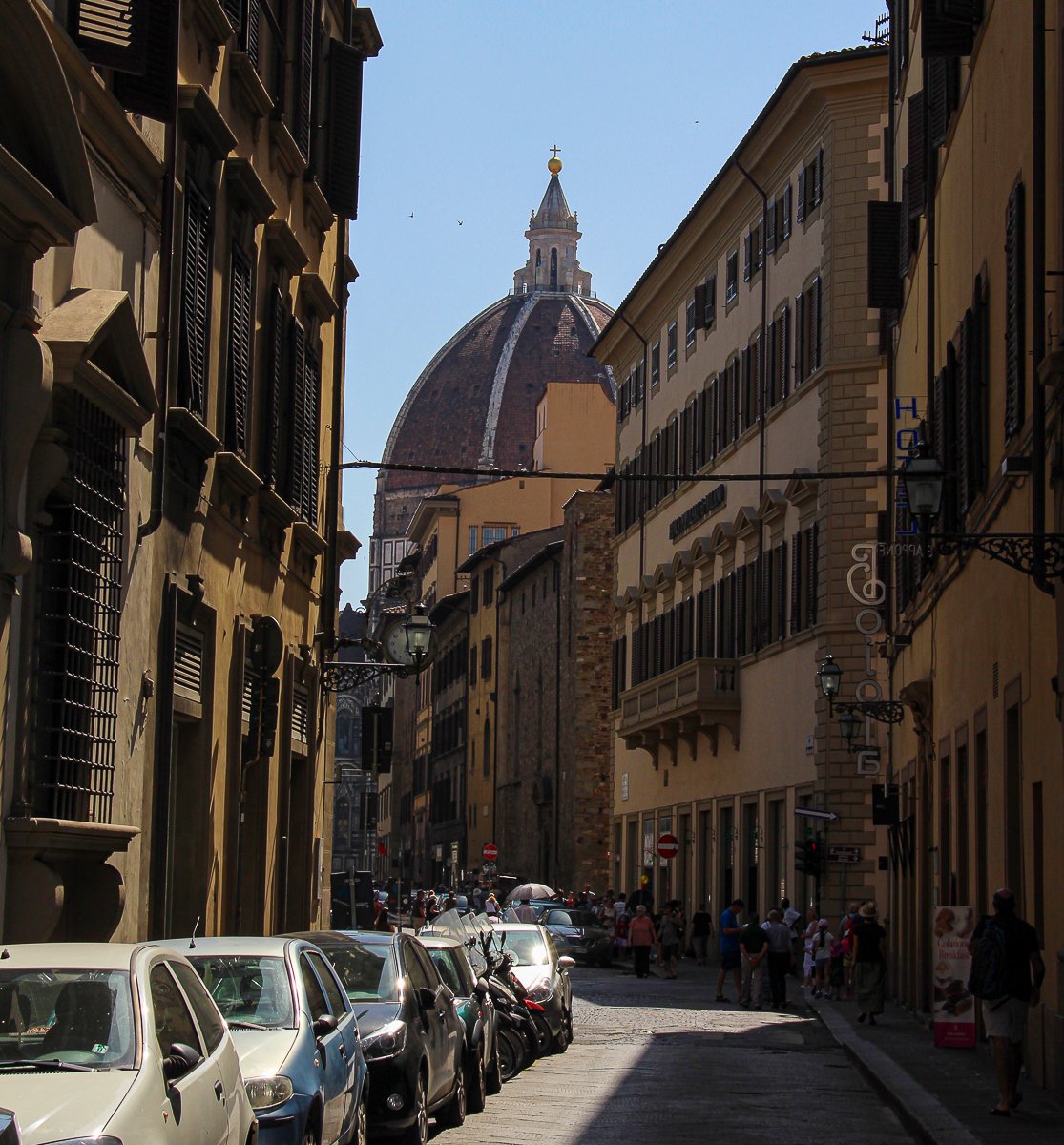 Busy street in Florence lined with cars and with people roaming around