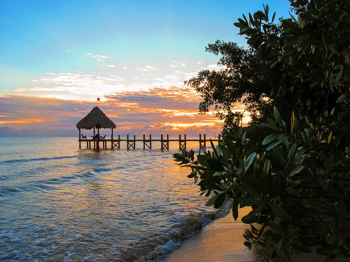 An amazing sunrise over a dock and palapa in Hopkins, Belize. Watching every sunrise and sunset is one of the best things to do in Belize!