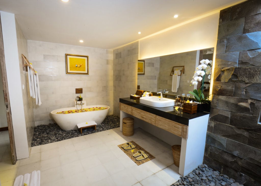 Spacious bathroom with elegant sink, wide mirror, and bathtub topped with beautiful flowers at Purana Boutique Resort where I stayed during my one week in Ubud
