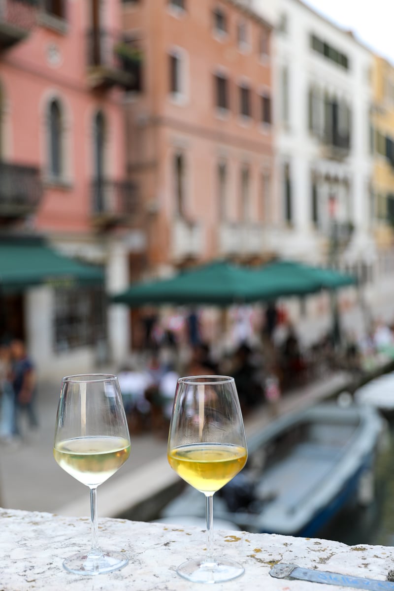 Two glasses of wine sitting atop a bridge ledge in Venice - sipping natural wine at Vino Vero is a must-add activity for your 2 days in Venice itinerary.