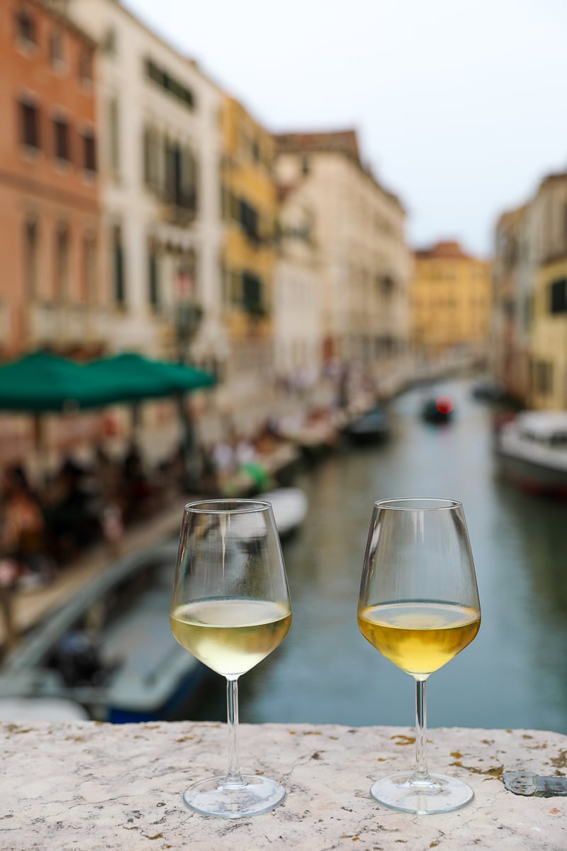 Two glasses of wine on the ledge of a bridge, overlooking a canal, in Venice