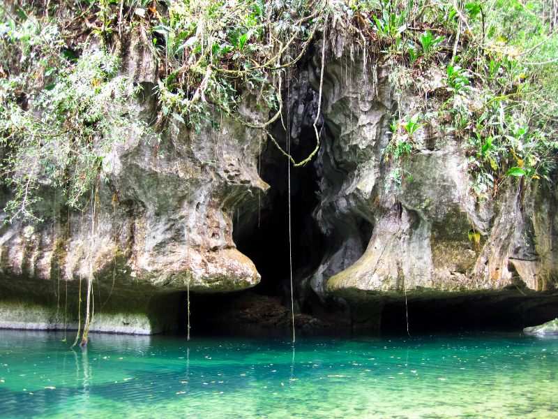 Outside rock wall of the Barton Creek Cave and turquoise river flowing in