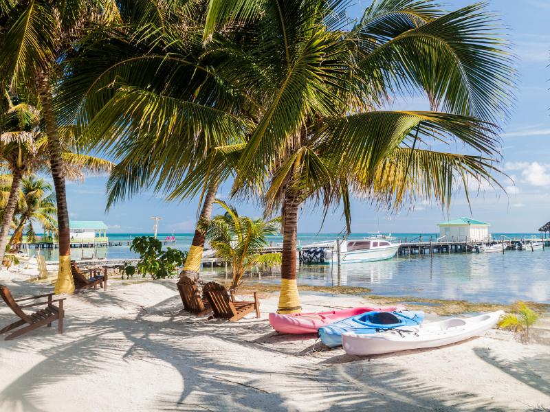 Colorful kayaks, wooden chairs, and palm trees on a white sand beach in Caye Caulker. In this Belize travel guide, you'll find the best places to visit including the beautiful island of Caye Caulker.