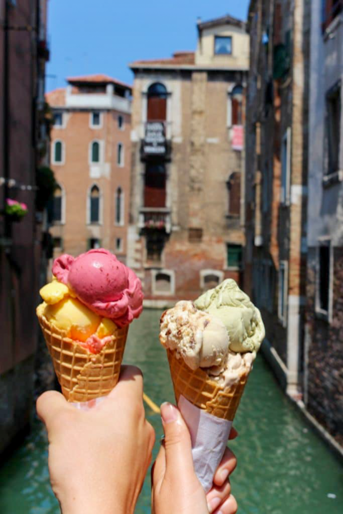 Two cones of colorful gelato with a canal in the background in Venice