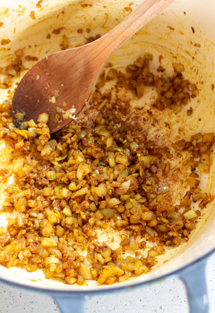Stirring onions and spices in a pot to make vegan cauliflower tikka masala.