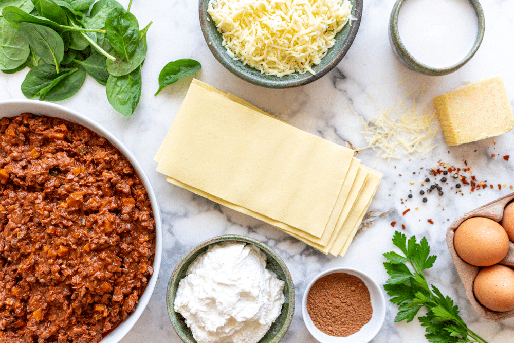 The ingredients to make the best vegetarian lasagna bolognese include a pot of vegan bolognese sauce, pasta sheets, ricotta cheese, spinach, mozzarella cheese, and more.