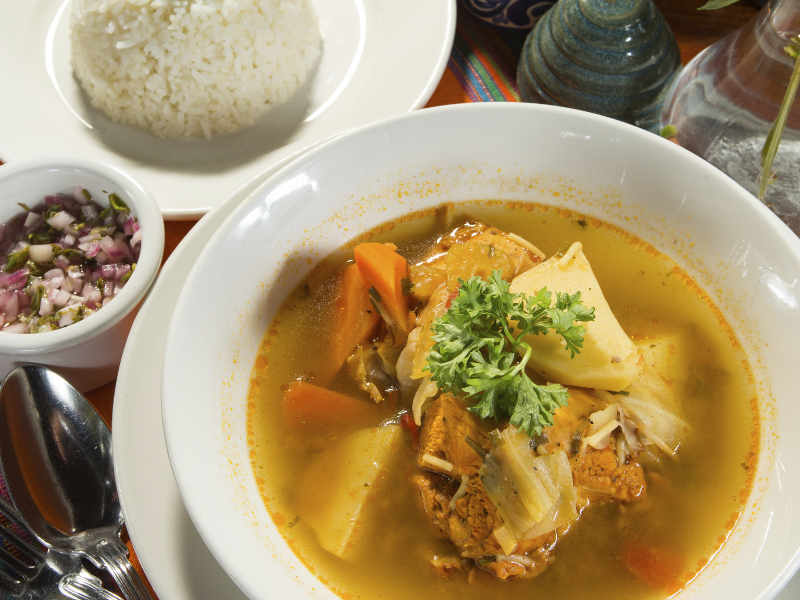 A hearty bowl of traditional soup in Belize with sides of rice and salsa.